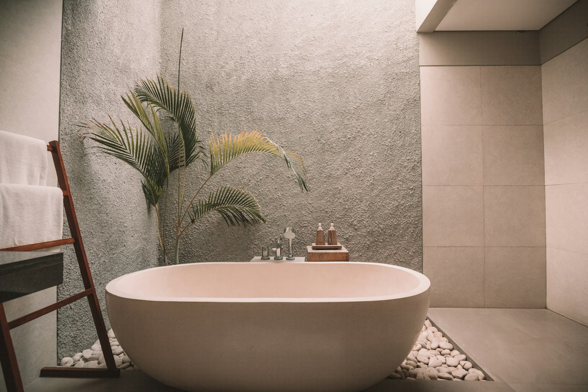 Freestanding oval soaking tub surrounded by river stones and palm plant.