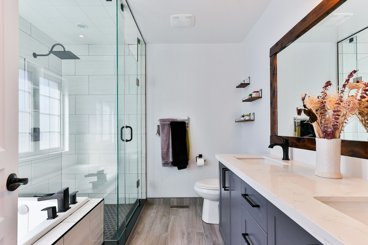 Custom walk-in shower with frameless glass enclosure, matte black fixtures, rainfall shower head, and modern vanity in San Diego.