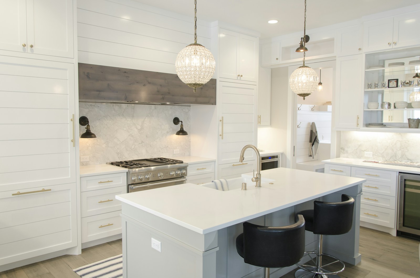 Bright white luxury kitchen with crystal globe pendants, center island with stools, and commercial gas range.