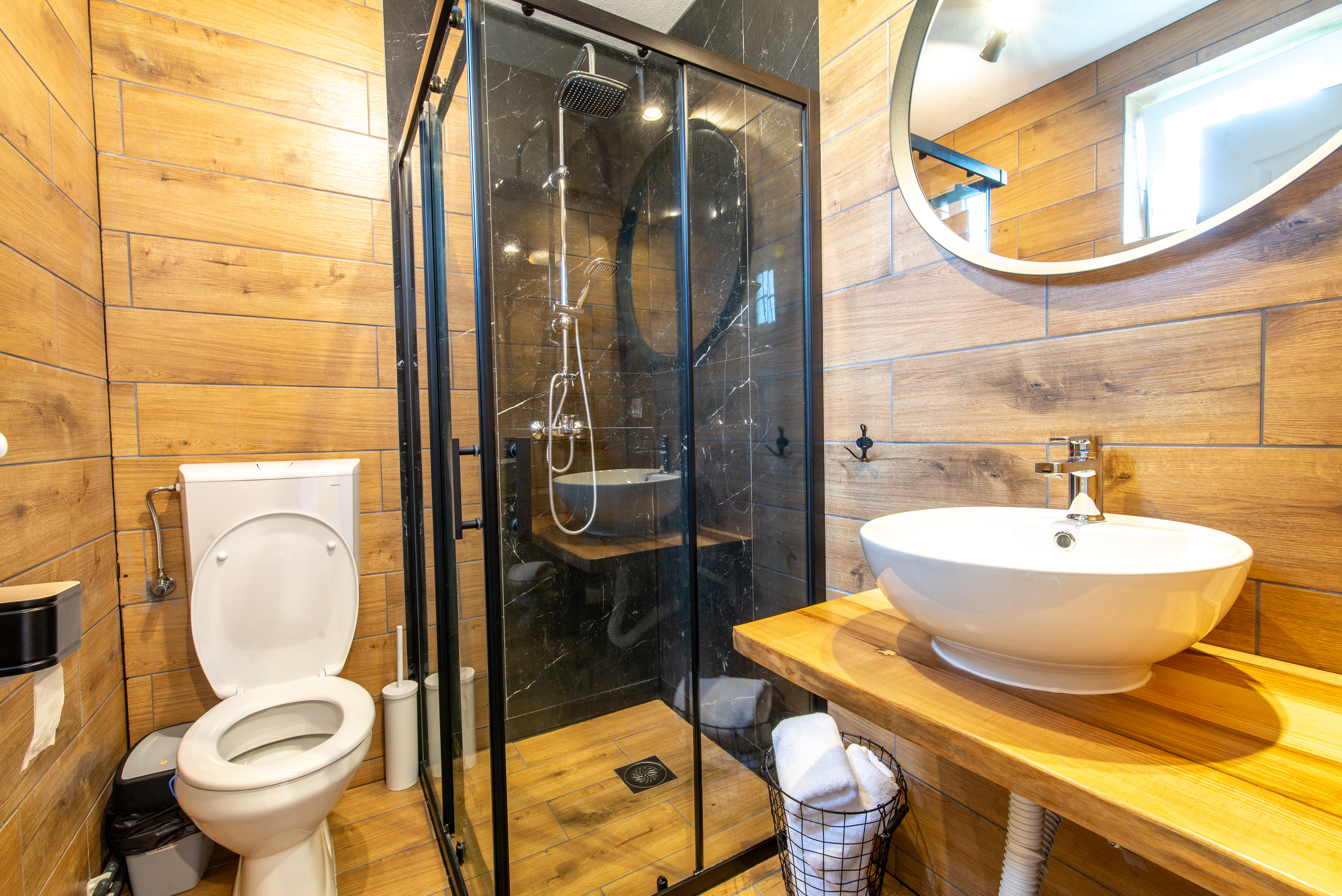Custom walk-in shower with black framed glass enclosure, rainfall shower head, and wood-look porcelain tile.