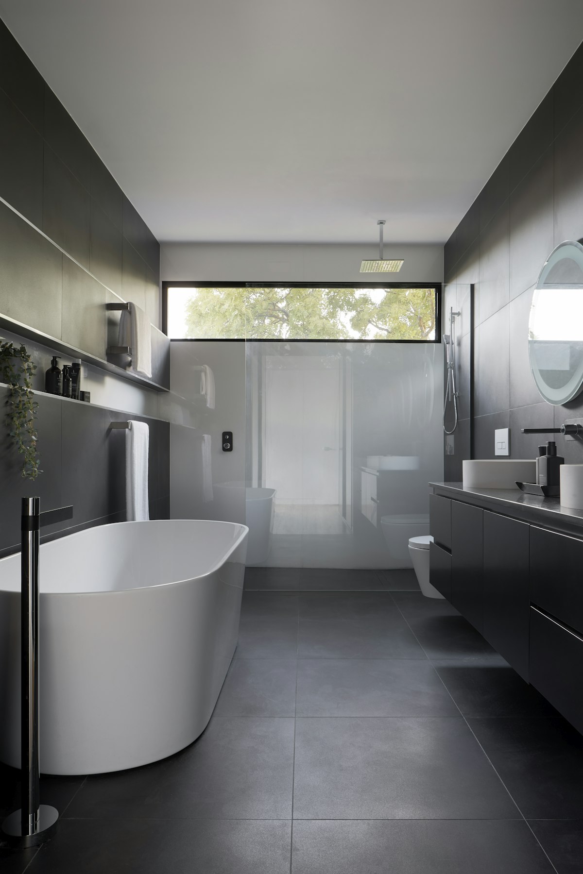 Modern master bathroom with open curbless wet room in back, freestanding soaking tub, and dark floating vanity.
