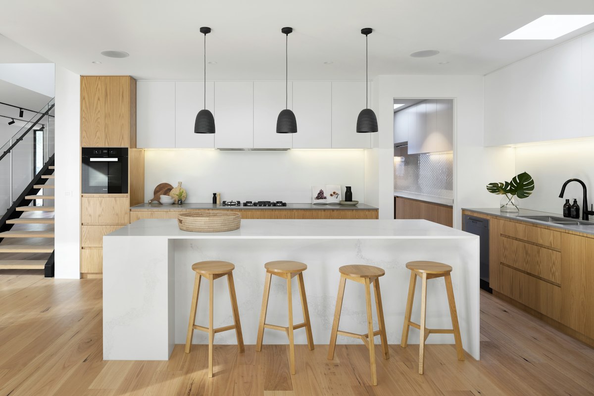 Modern open-concept kitchen featuring an expansive white marble waterfall island, 4 wooden stools, and natural oak cabinets in San Diego.